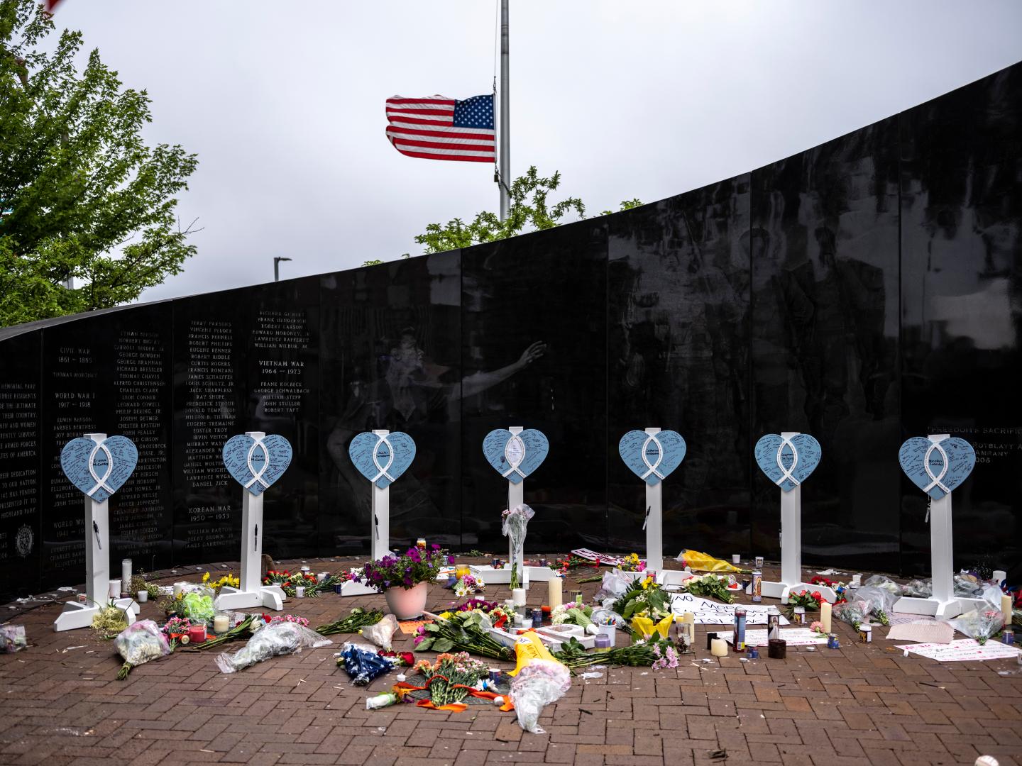A memorial for the seven victims of the Highland Park, Illinois shooting, with a blue heart on a while pole for each of the lives lost.