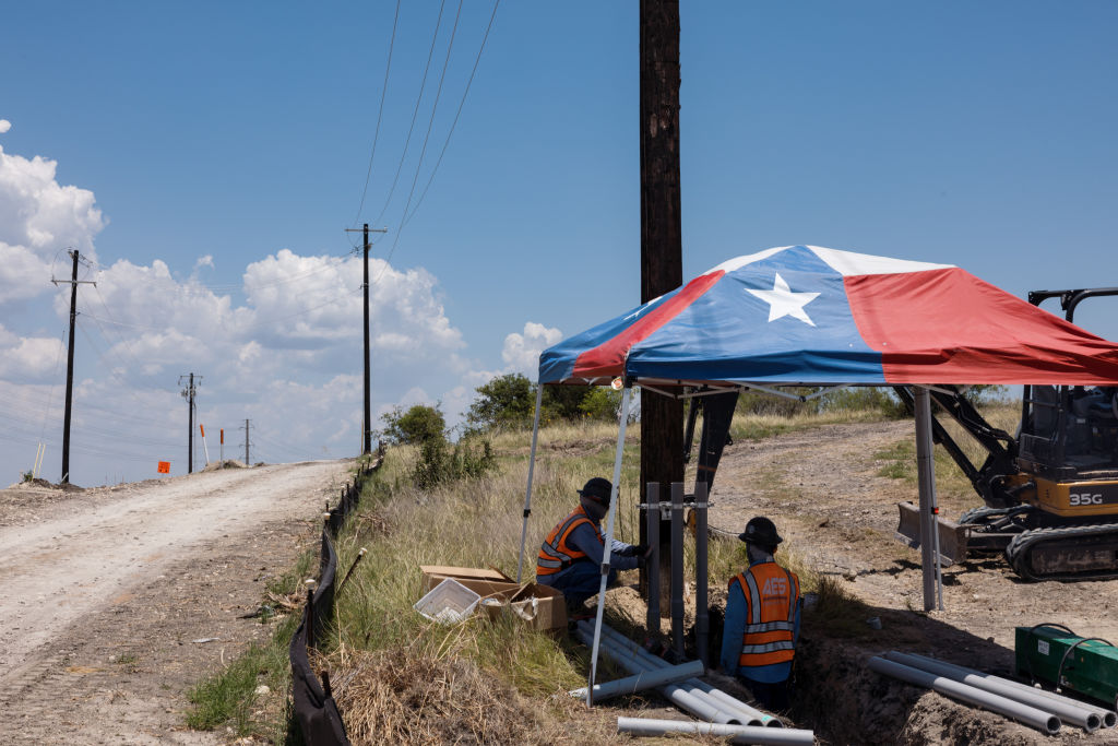 Workers install infrastructure under a Texas flag–themed tent during a heat wave in Austin, on July 11, 2022. Texas residents and businesses are being asked to conserve electricity during a heat wave that’s expected to stretch the state’s grid.