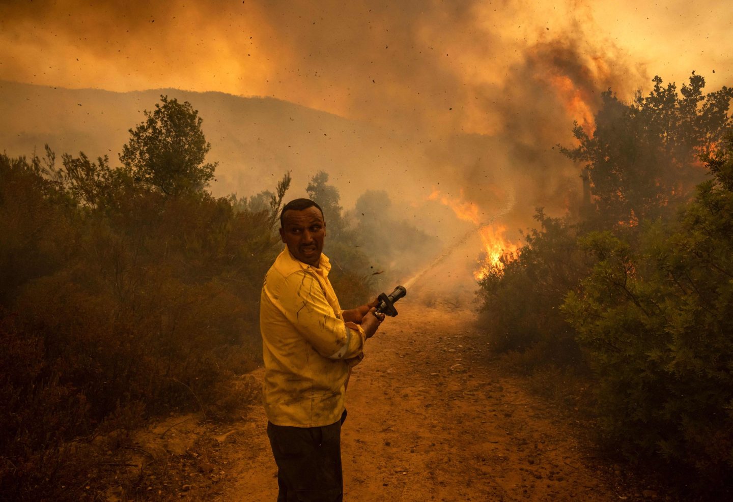 A forest ranger sprays water from a hose on a forest fire near the Moroccan city of Ksar el-Kebir in the Larache region, on July 15, 2022. (