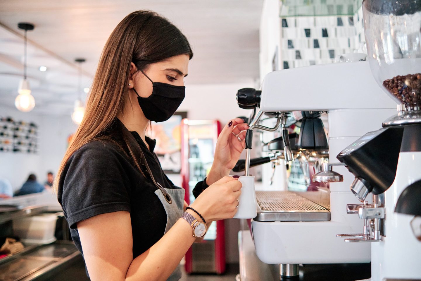 Young waiter with protective mask using a coffee machine