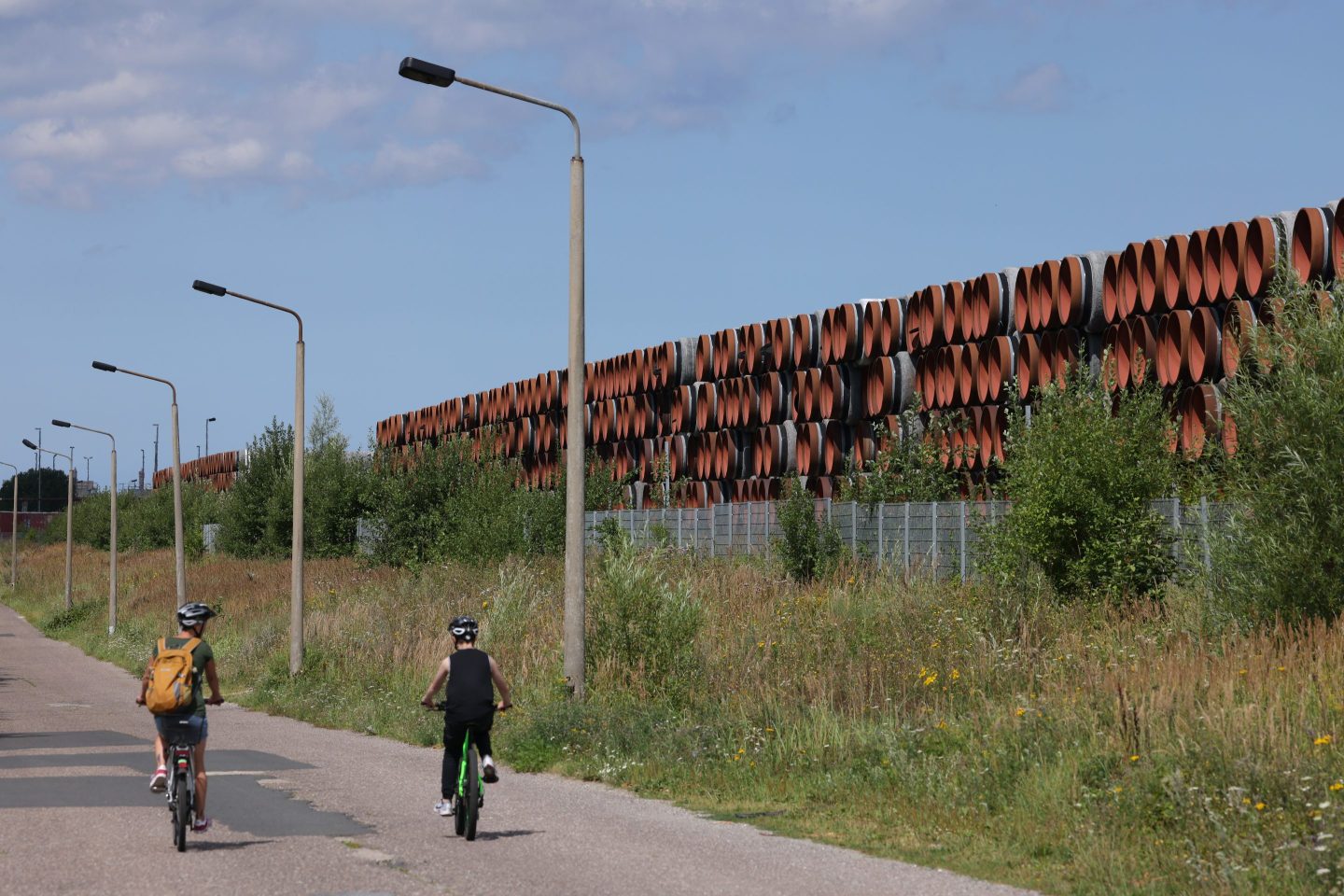 Photo of people riding bicycles in front of sections of pipe for the Nord Stream 2 gas pipeline on August 4, 2021, in Sassnitz, Germany.