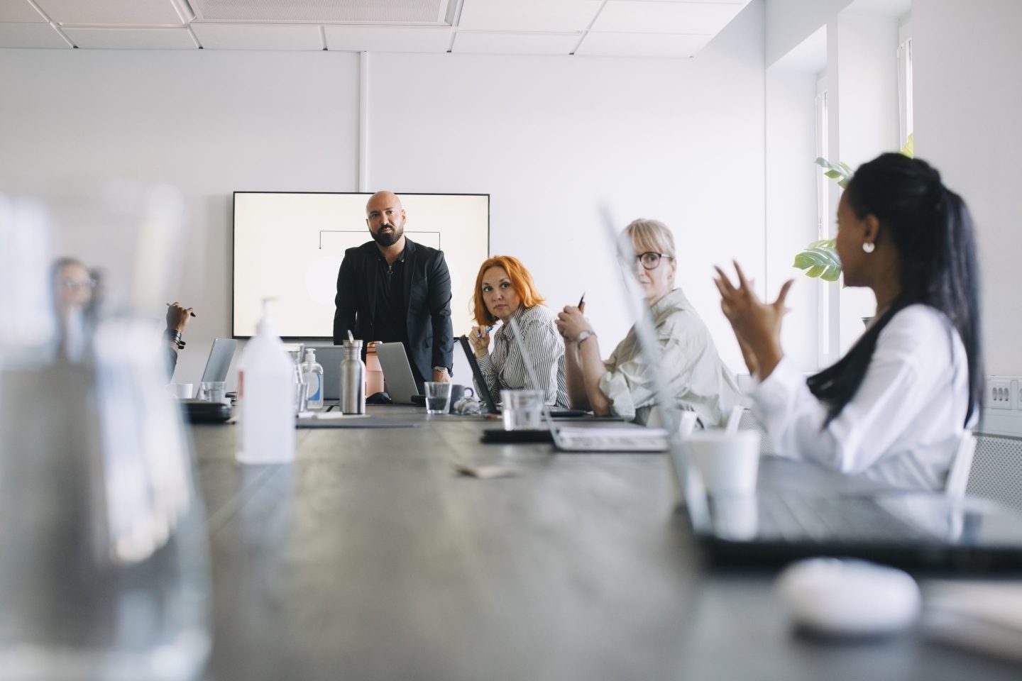 A woman at the end of a long table addresses the other people at the table during a board meeting.