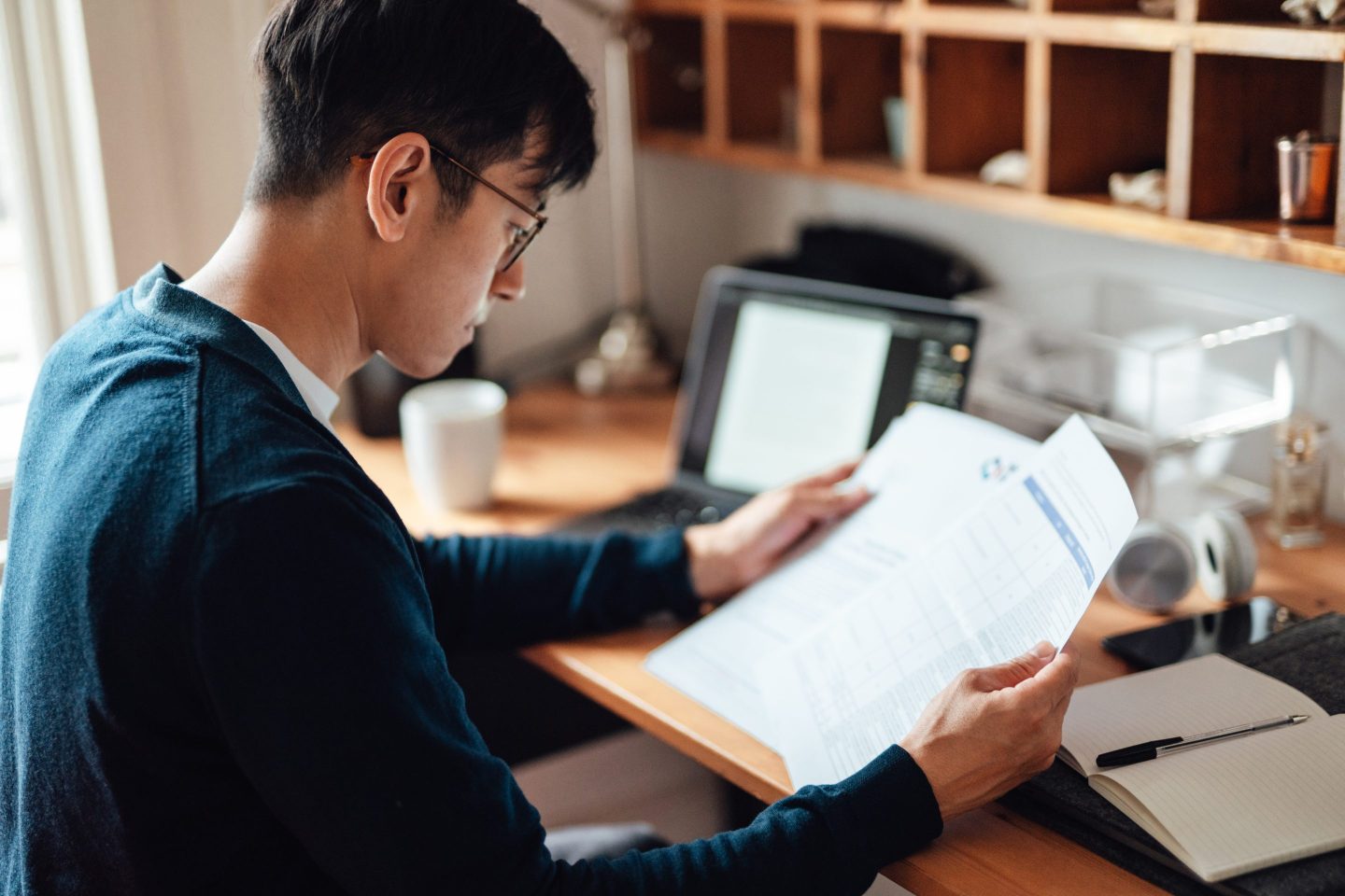 Young Asian man looking at financial bills while working on laptop at home
