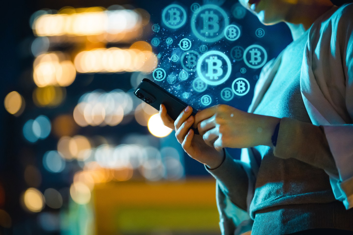 A young Asian woman using her smartphone in the city at night to invest in Bitcoin