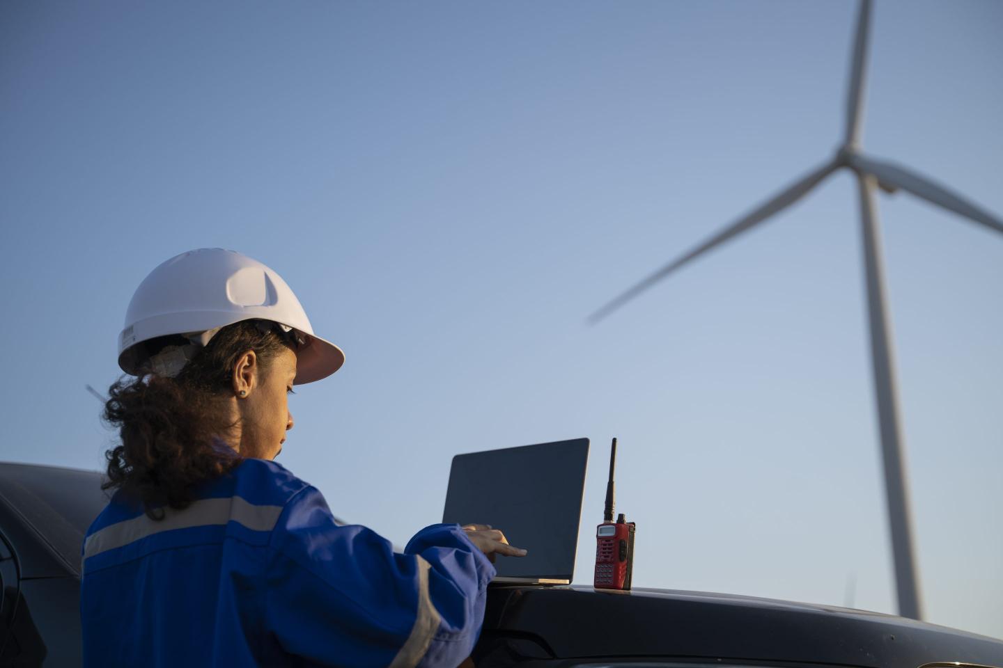 Female engineer working on wind farm, using laptop.