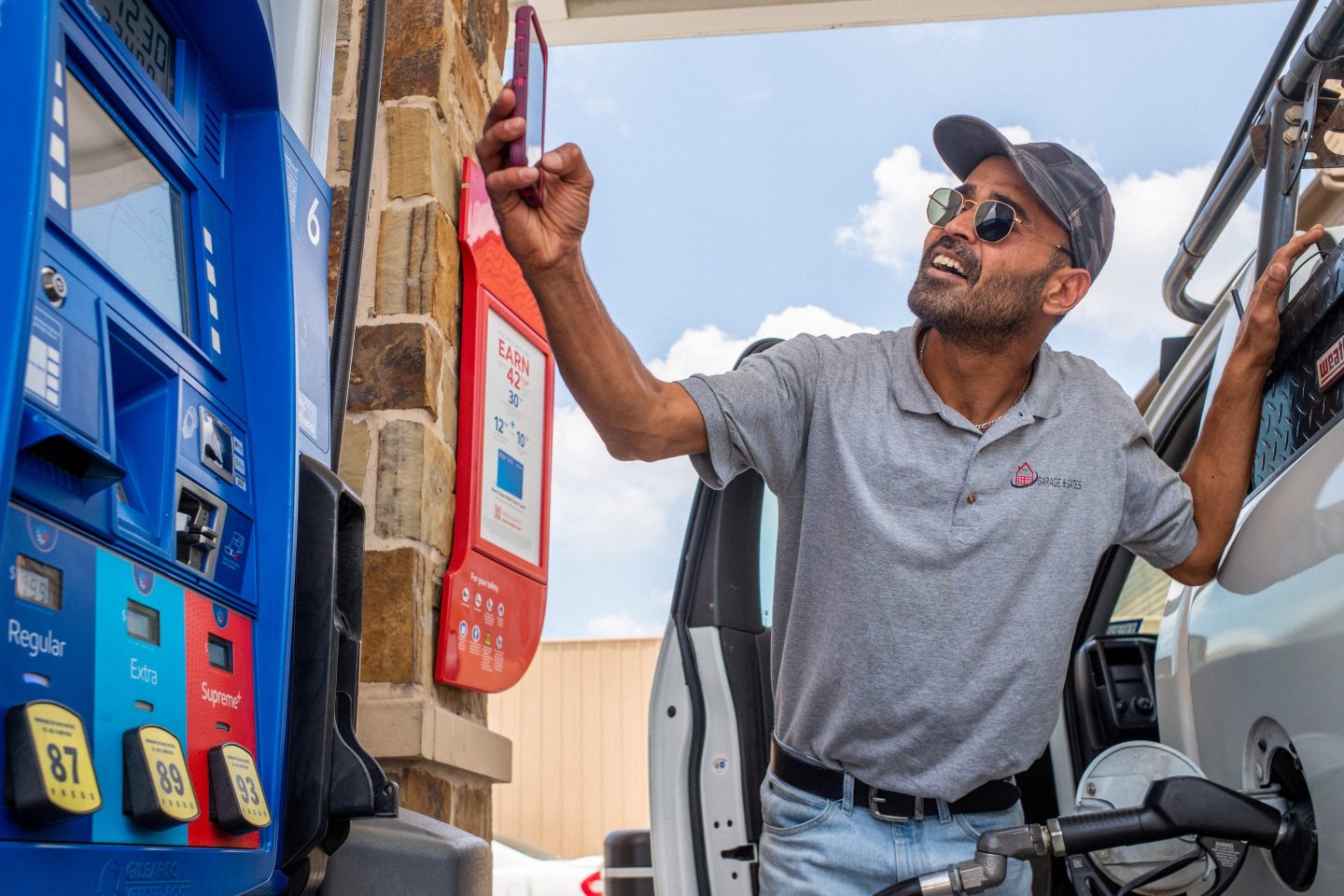A man takes a picture of gas prices as he pumps his gas.