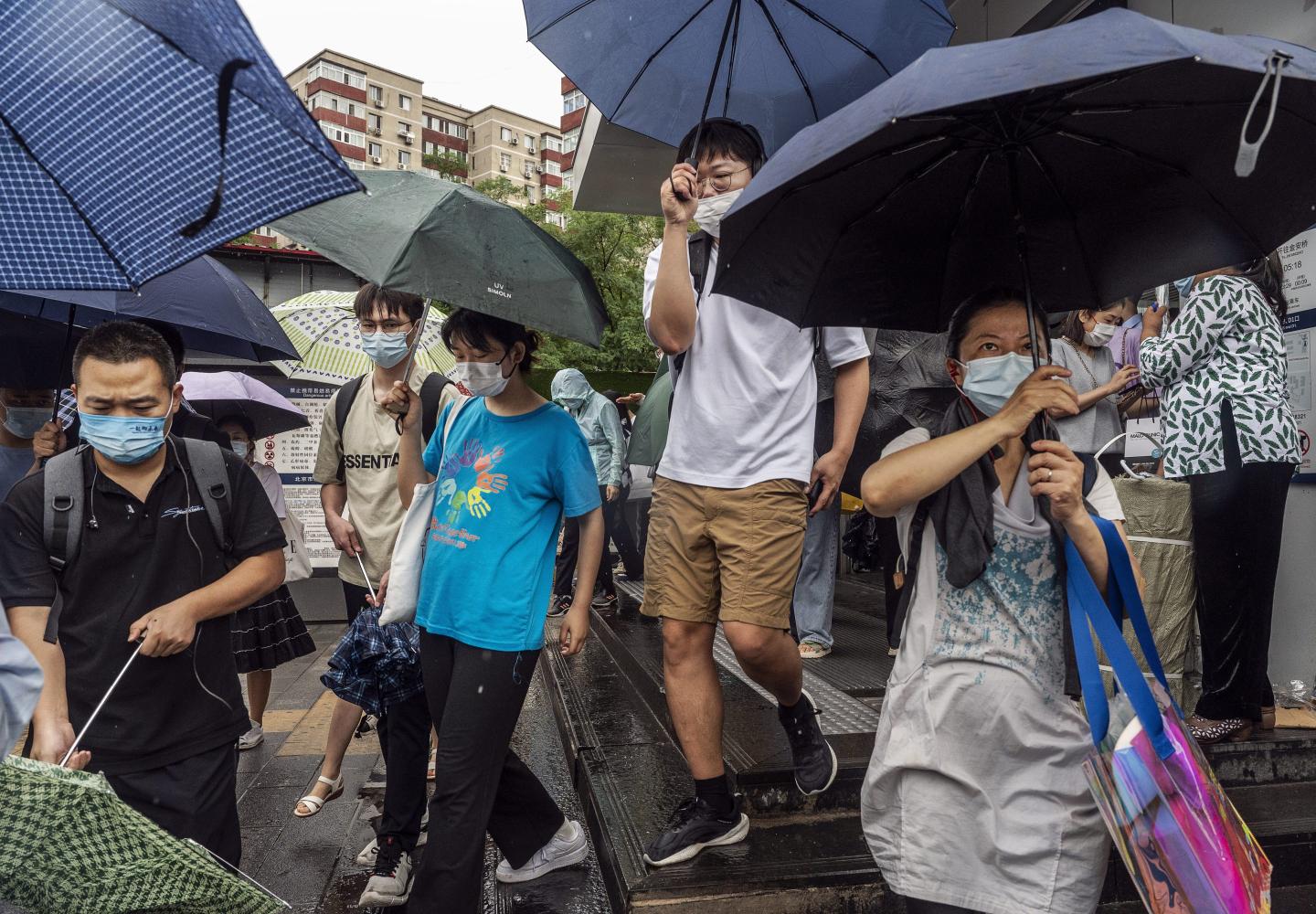 Masked Beijing residents open umbrellas after leaving a subway station