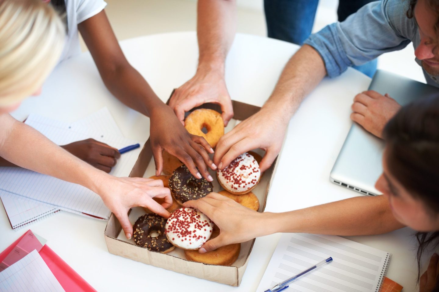 Photo of a box of doughnuts with people reaching for them