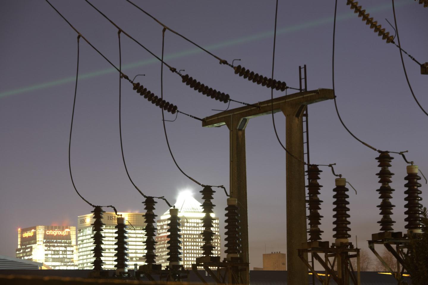 As evening light fades, bright light from the electricity-hungry Canary Wharf docklands development is supplied by the voltage from electricity cables and supporting struts at West Ham sub-station, Canning Town, London England