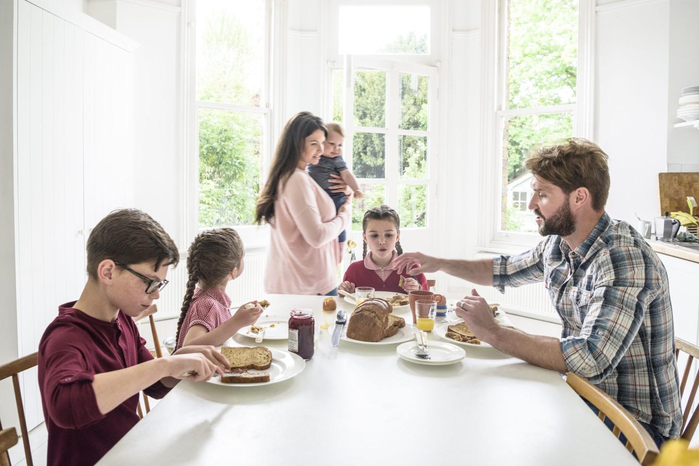 Dining table in modern home with family eating breakfast, mother carrying son