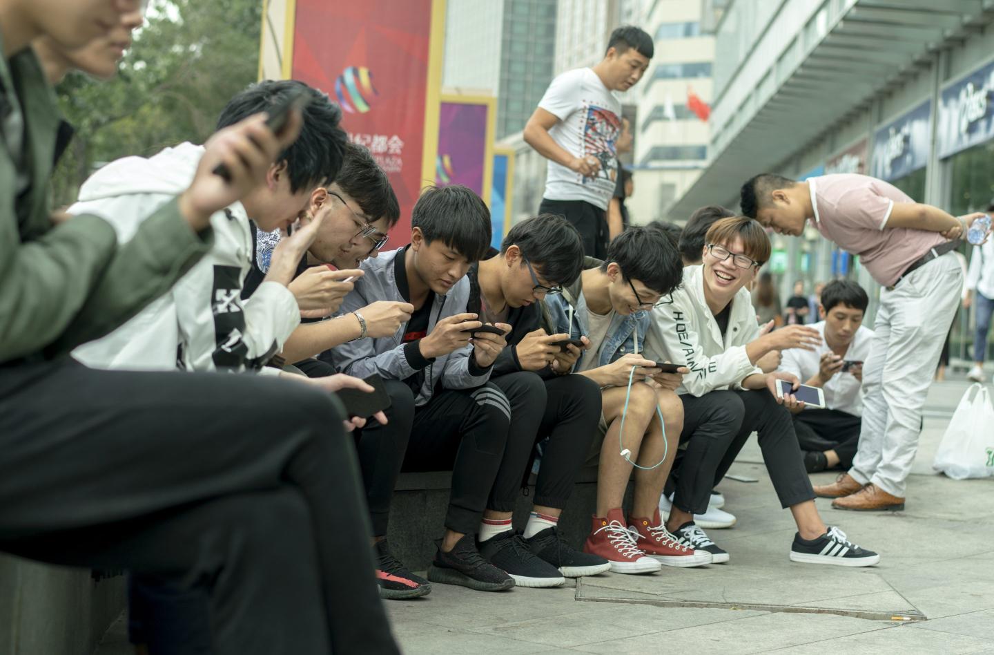 Young Chinese gamers play on their mobile phones outside a shopping mall.
