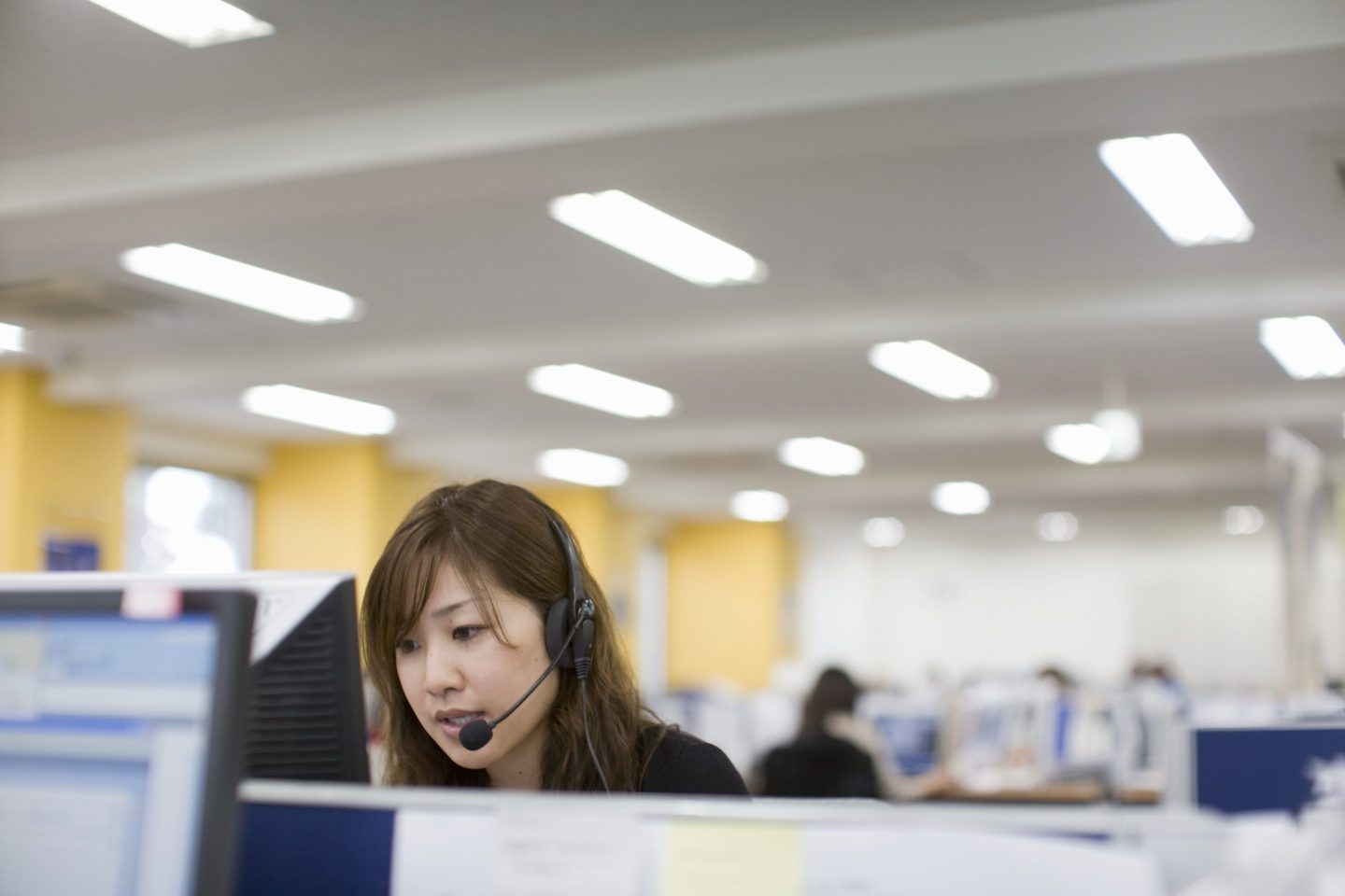 Woman talking with headset in front PC in office