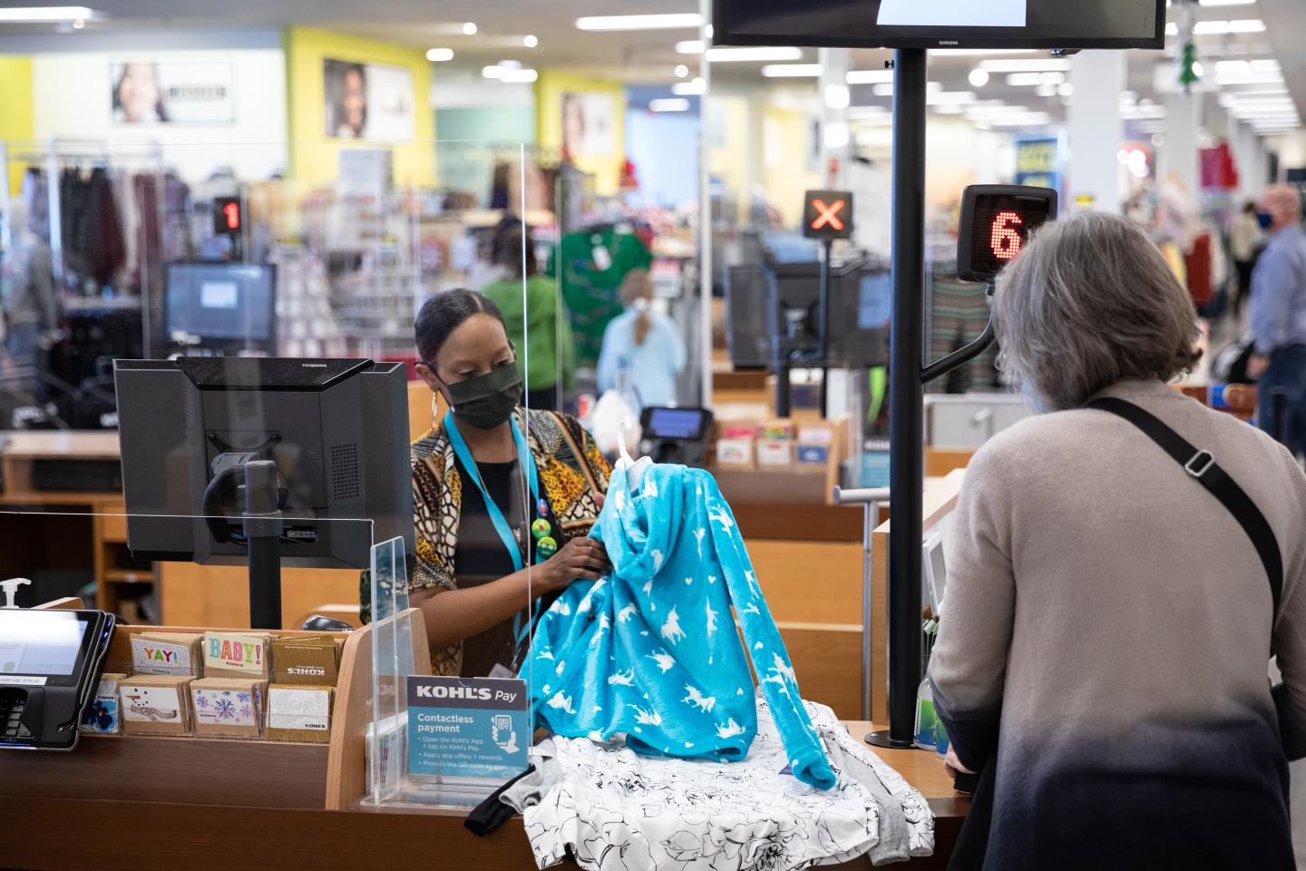 An employee wearing a protective masks assists a customer at the checkout counter at a Kohl's department store.