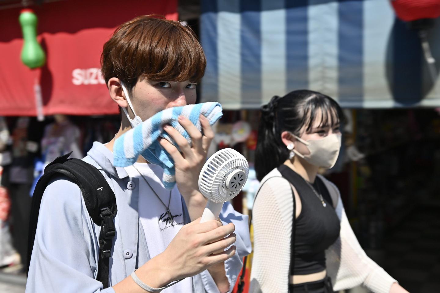 A man walks on the street using a towel and a portable fan to protect himself from the sun and the heat on June 30 2022, in Tokyo's famous Asakusa district in Tokyo, Japan.