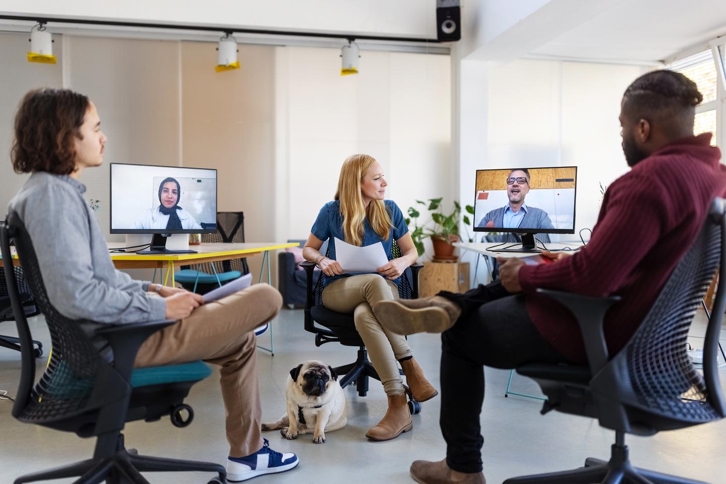 Team in office sitting in a room during a hybrid meeting with two remote employees.