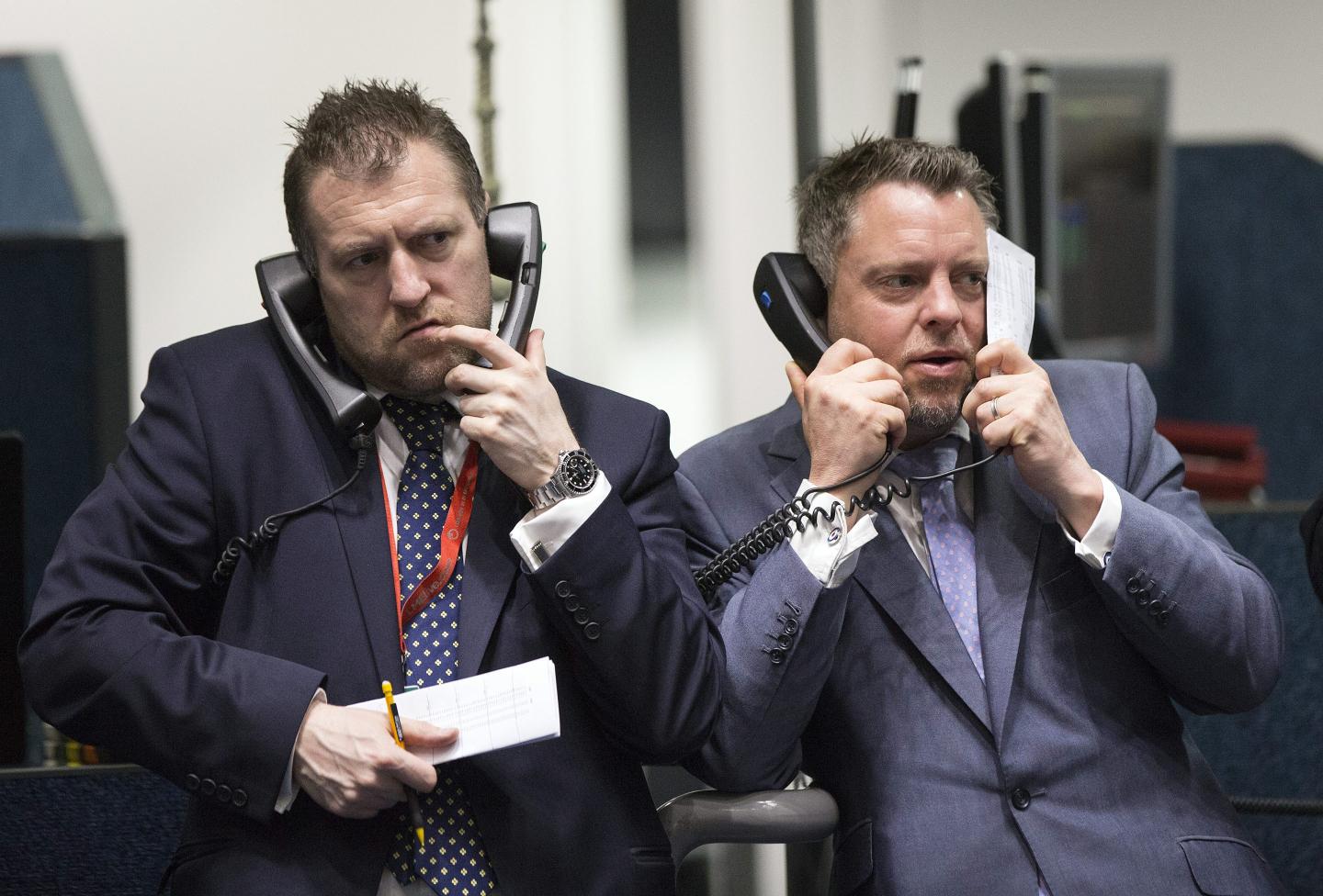 Two traders on the London Metals Exchange both holding two sets of telephone receivers, one held to each ear.