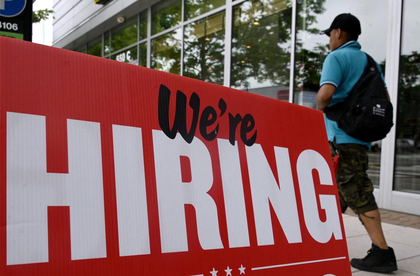 A man walks past a sign that says "now hiring."