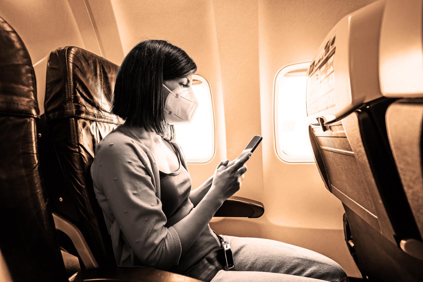 Woman wearing face mask is using smartphone in airplane