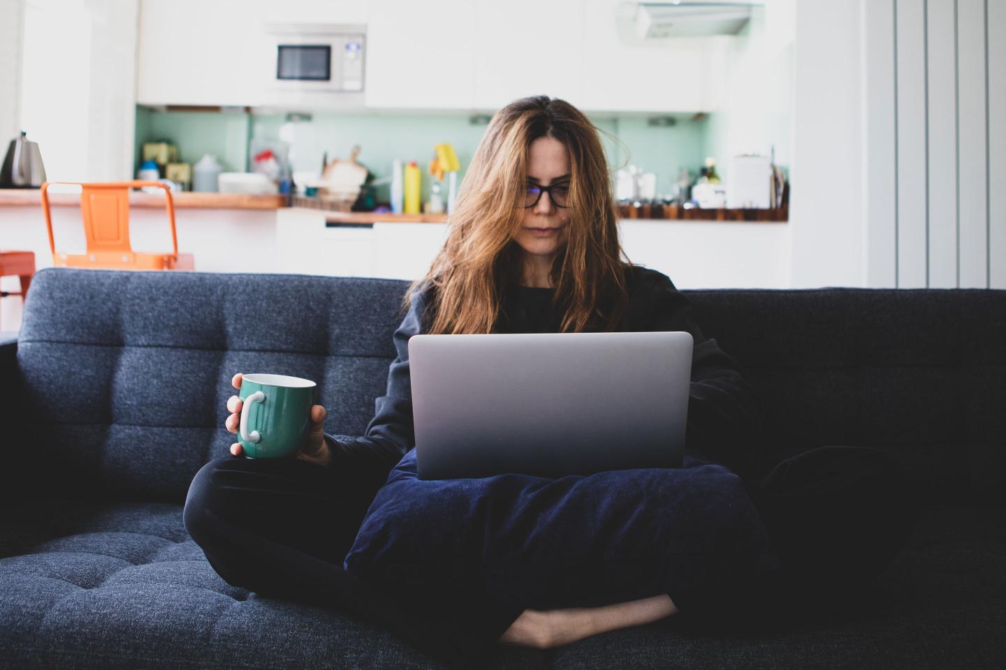 Woman using laptop on cushion, sitting on a sofa