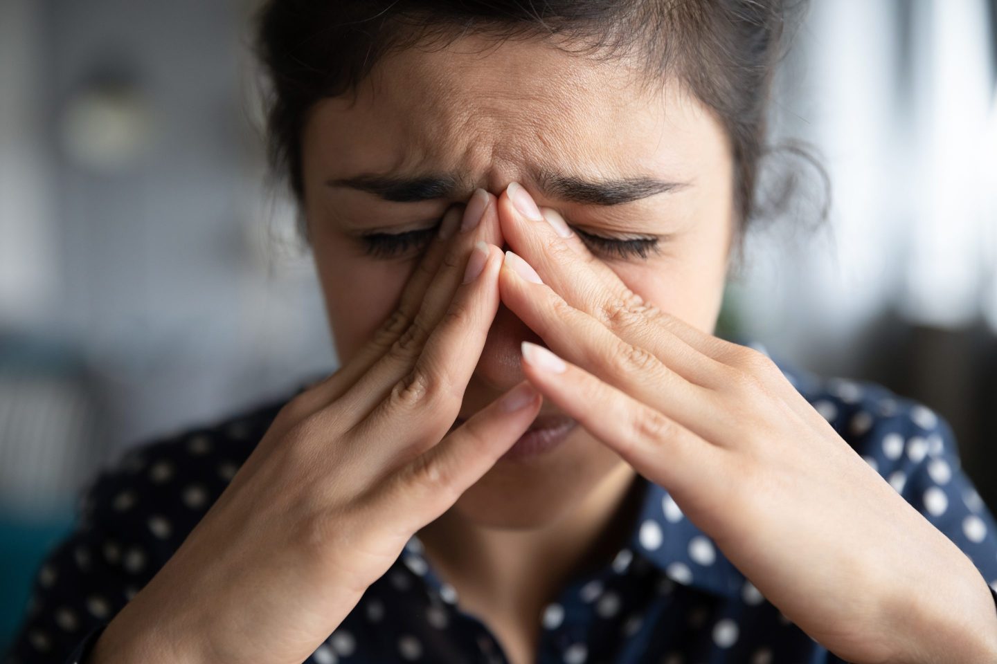 A close-up photo of a young woman who is upset, holding her face