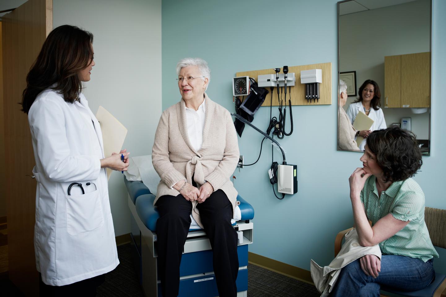Mature female patient sitting on exam table in discussion with doctor and daughter.