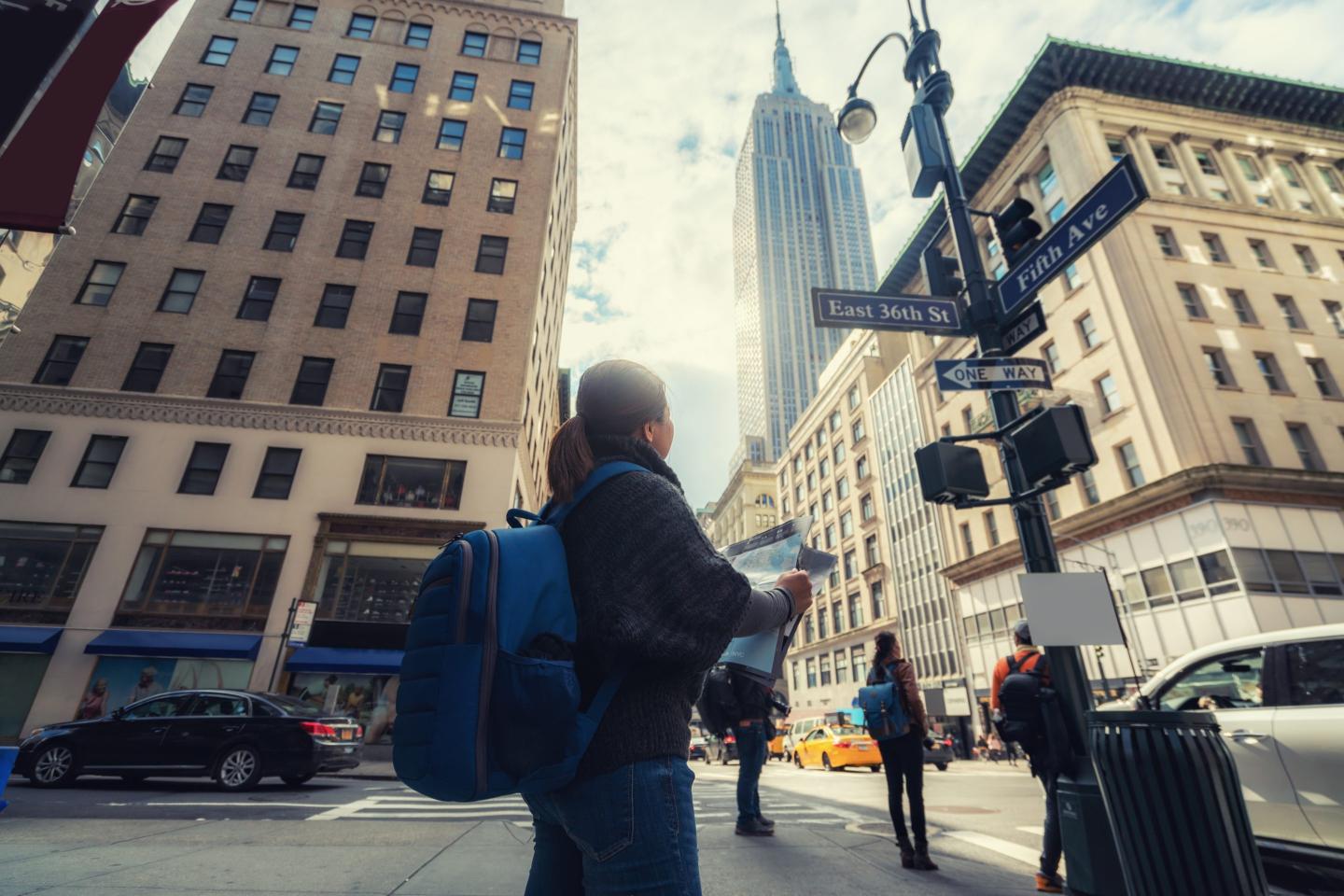 Asuan woman in New York looking at city map . Happy young woman enjoying the trip to New York and checking the map. Empire state tower on background