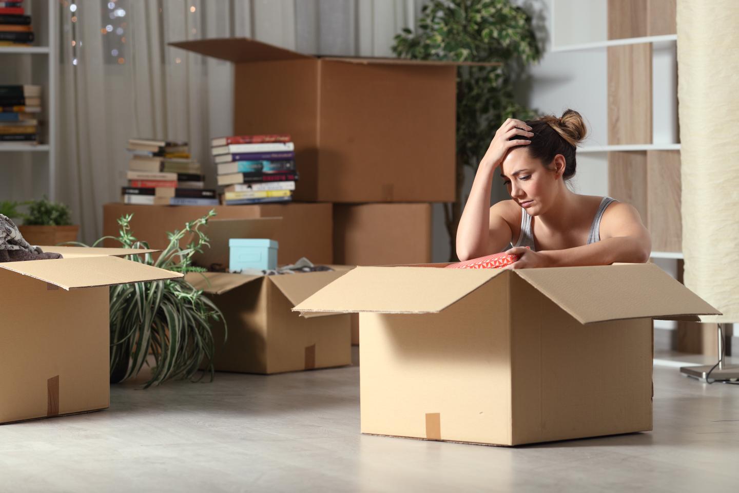 A sad woman resting near a moving box as she packs up her belongings.
