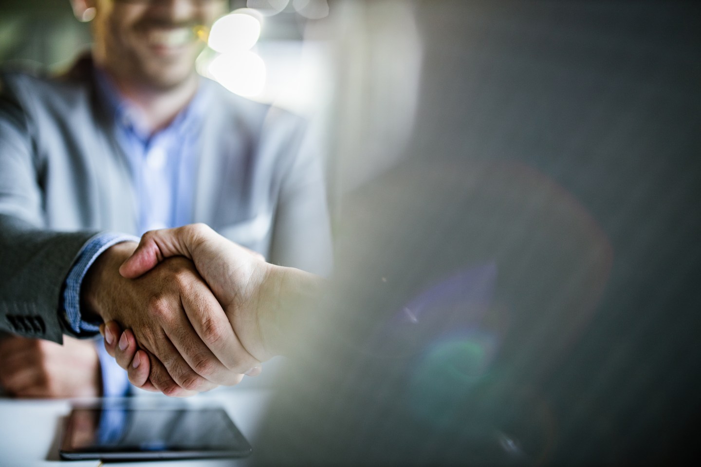 The image shows two people shaking hands in a business setting.