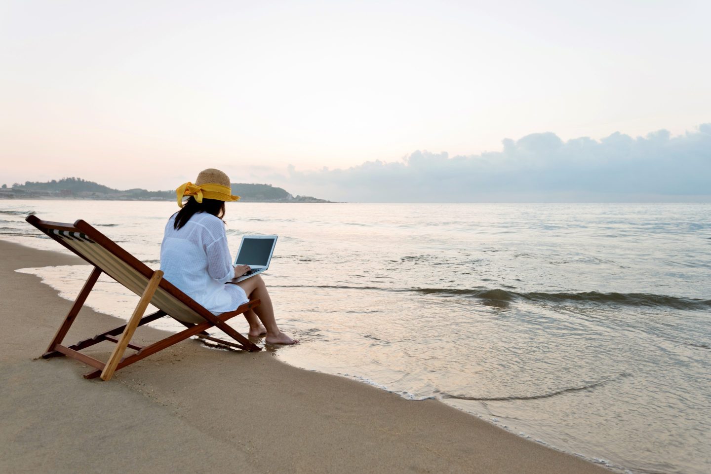 A woman sitting at the beach while working from her laptop