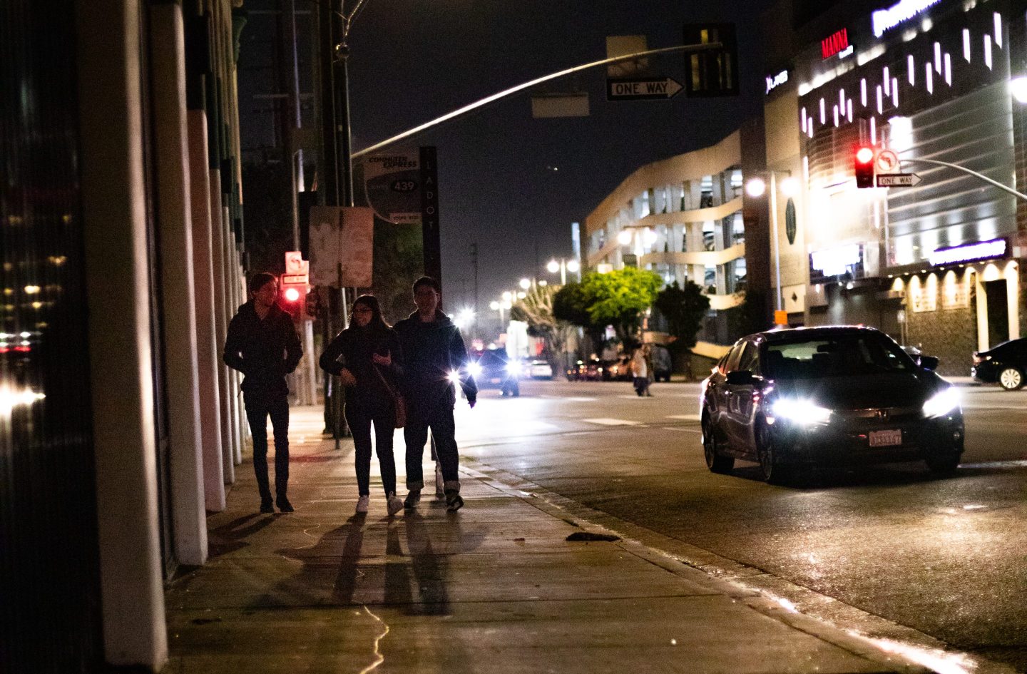 Pedestrians walk at night through downtown Los Angeles while a car drives by