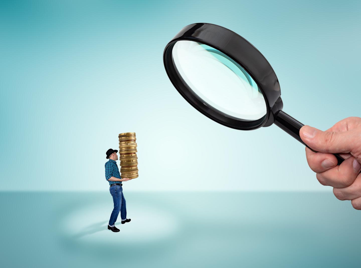 Man holding a stack of coins and big magnifying glass in hand