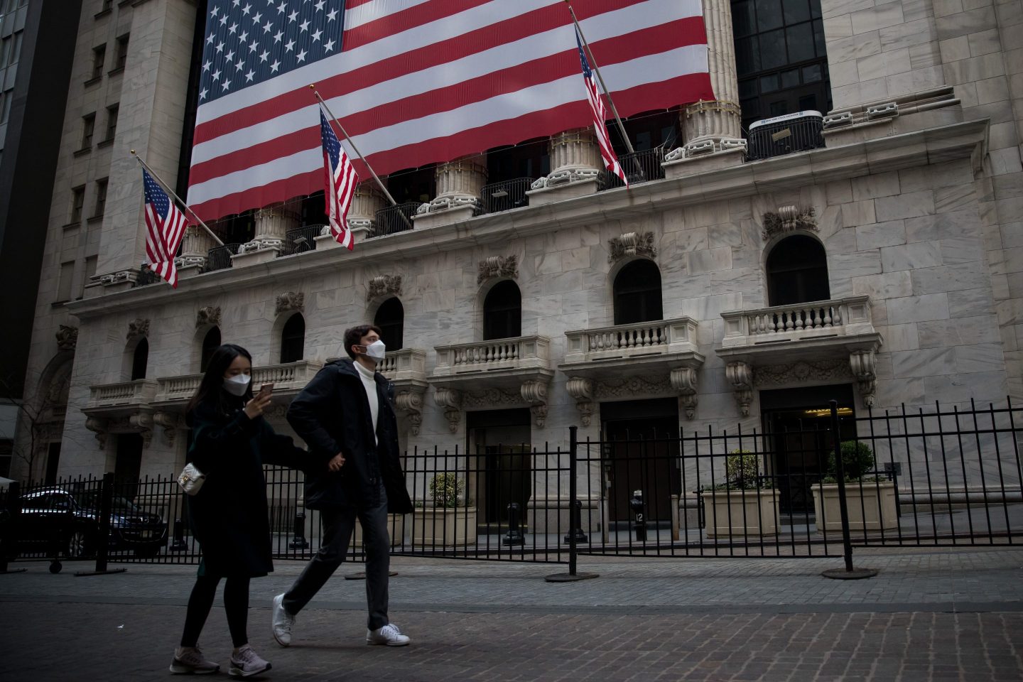 Pedestrians wearing face masks walk past the New York Stock Exchange in New York on March 18, 2020.