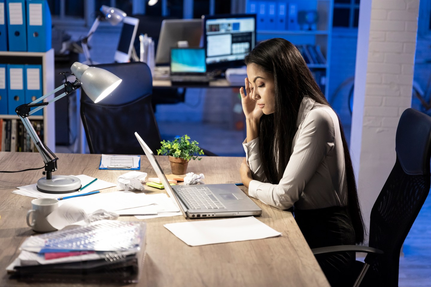 A young Asian woman working late and using laptop at workplace.