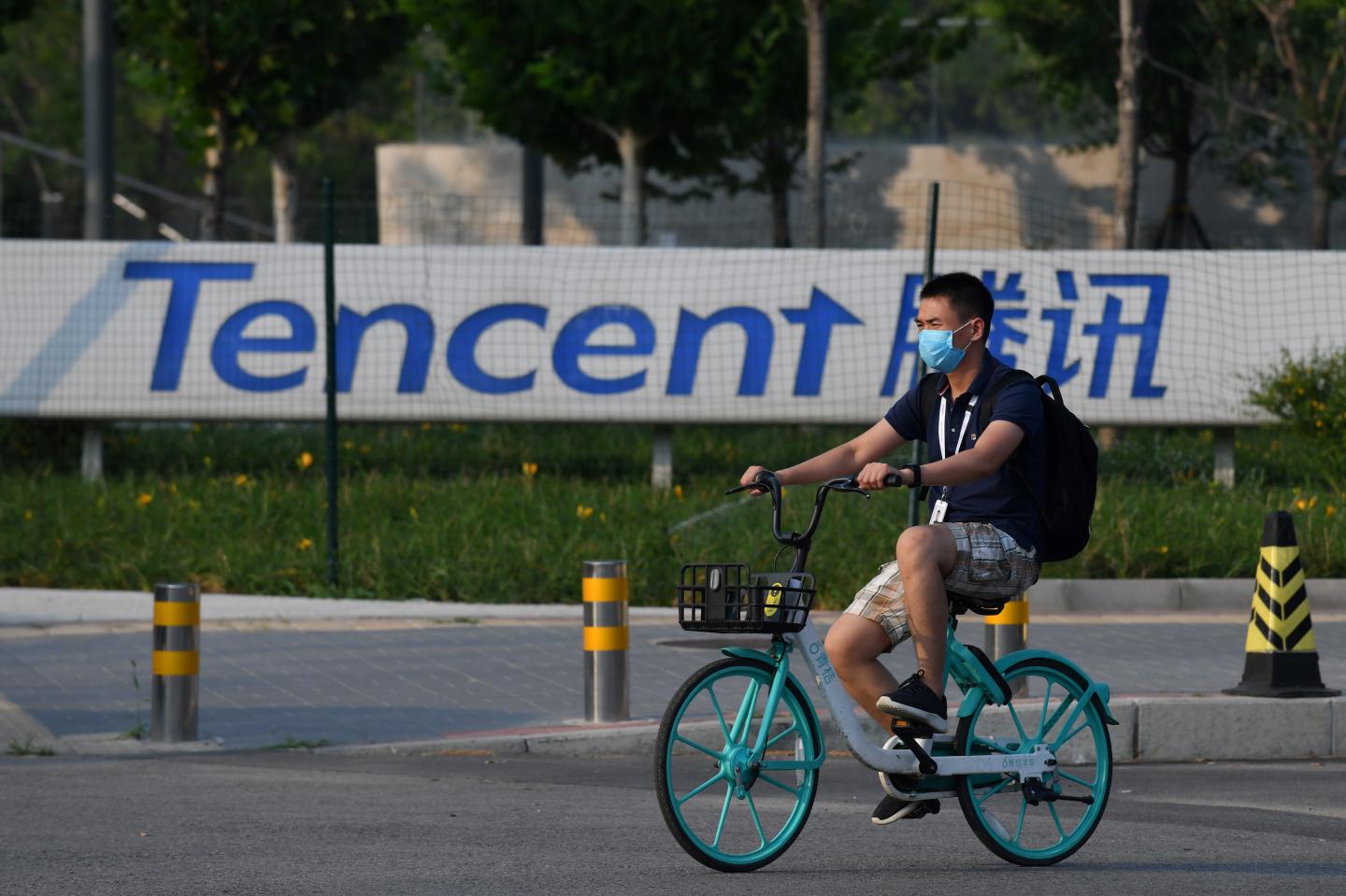 A man on a bike rides past a sign for Chinese company Tencent