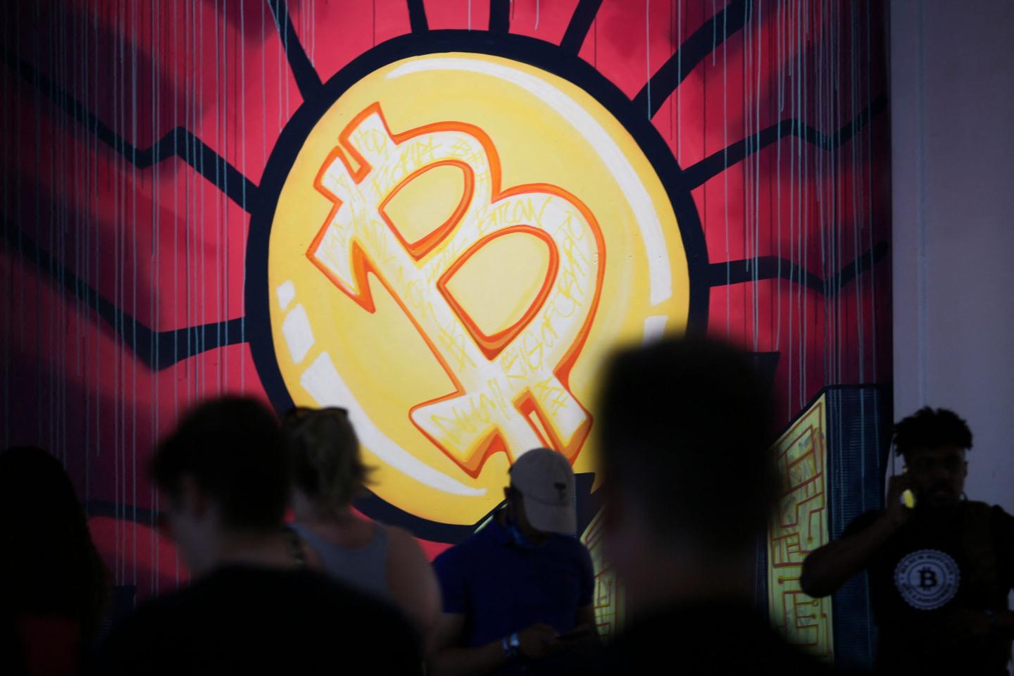 A banner of the Bitcoin logo is displayed at a currency conference in Miami