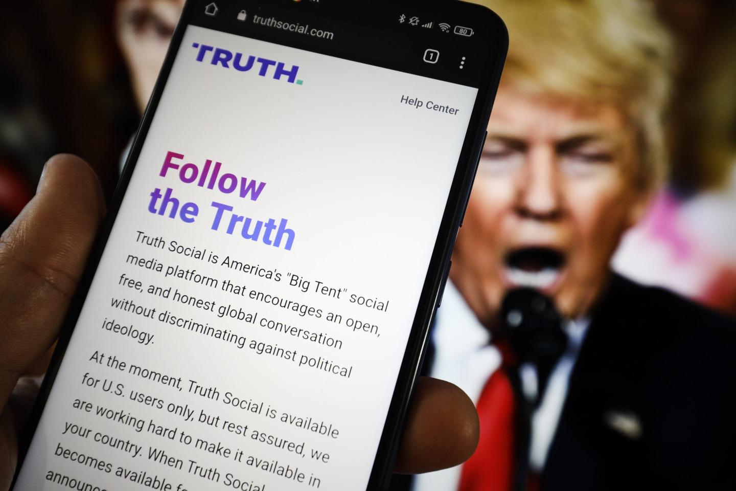The TRUTH Social website is seen on a mobile device with an image of former US president Donald Trump in the background
