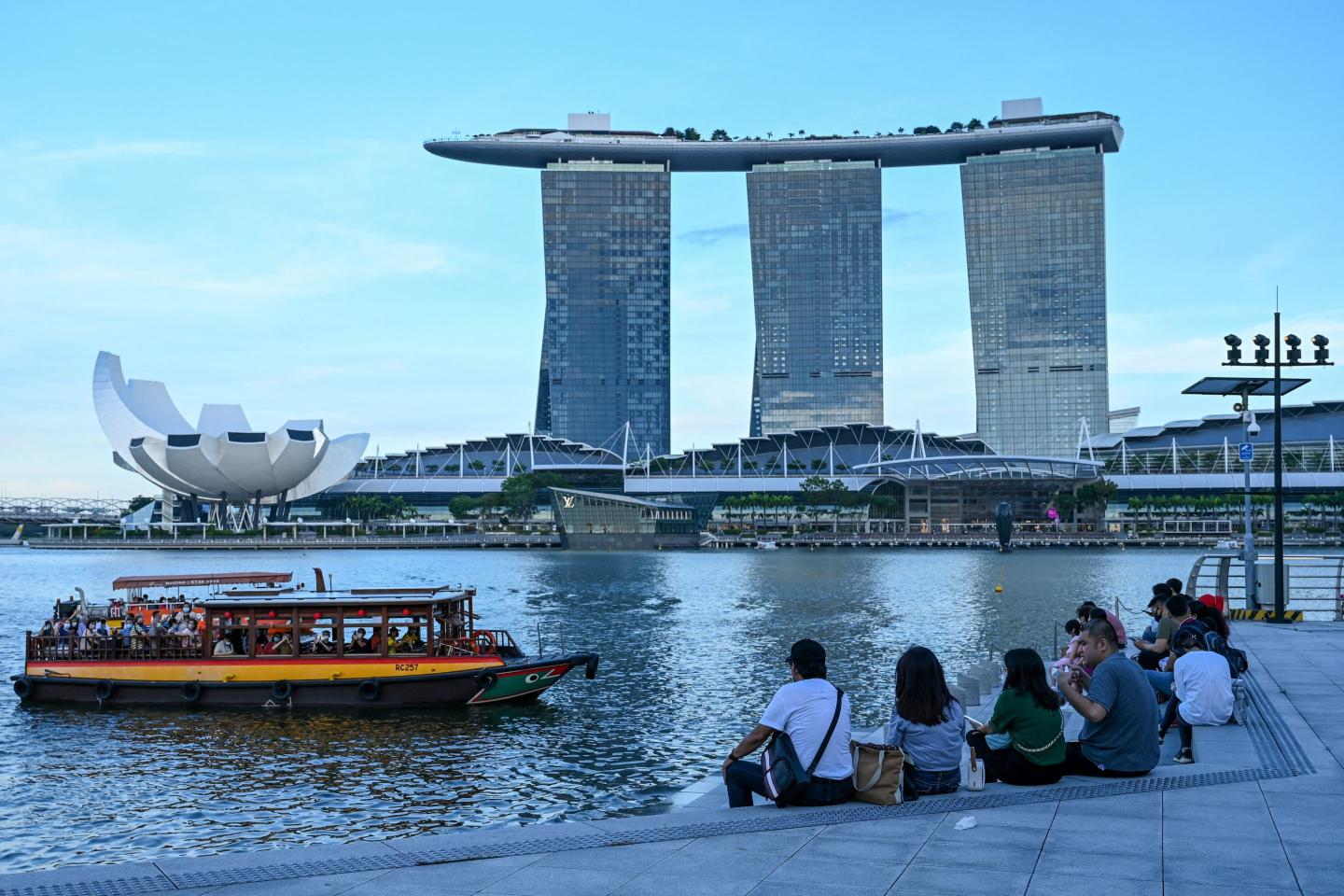 People sit along the promenade overlooking the Marina Bay Sands hotel and resort in Singapore in February 2022.