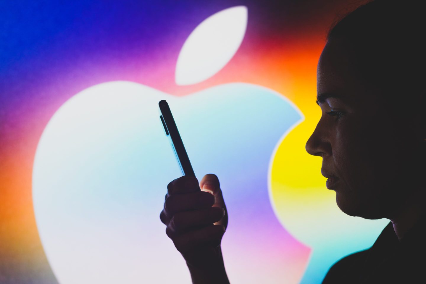 A person looking at a phone with the Apple logo on the background