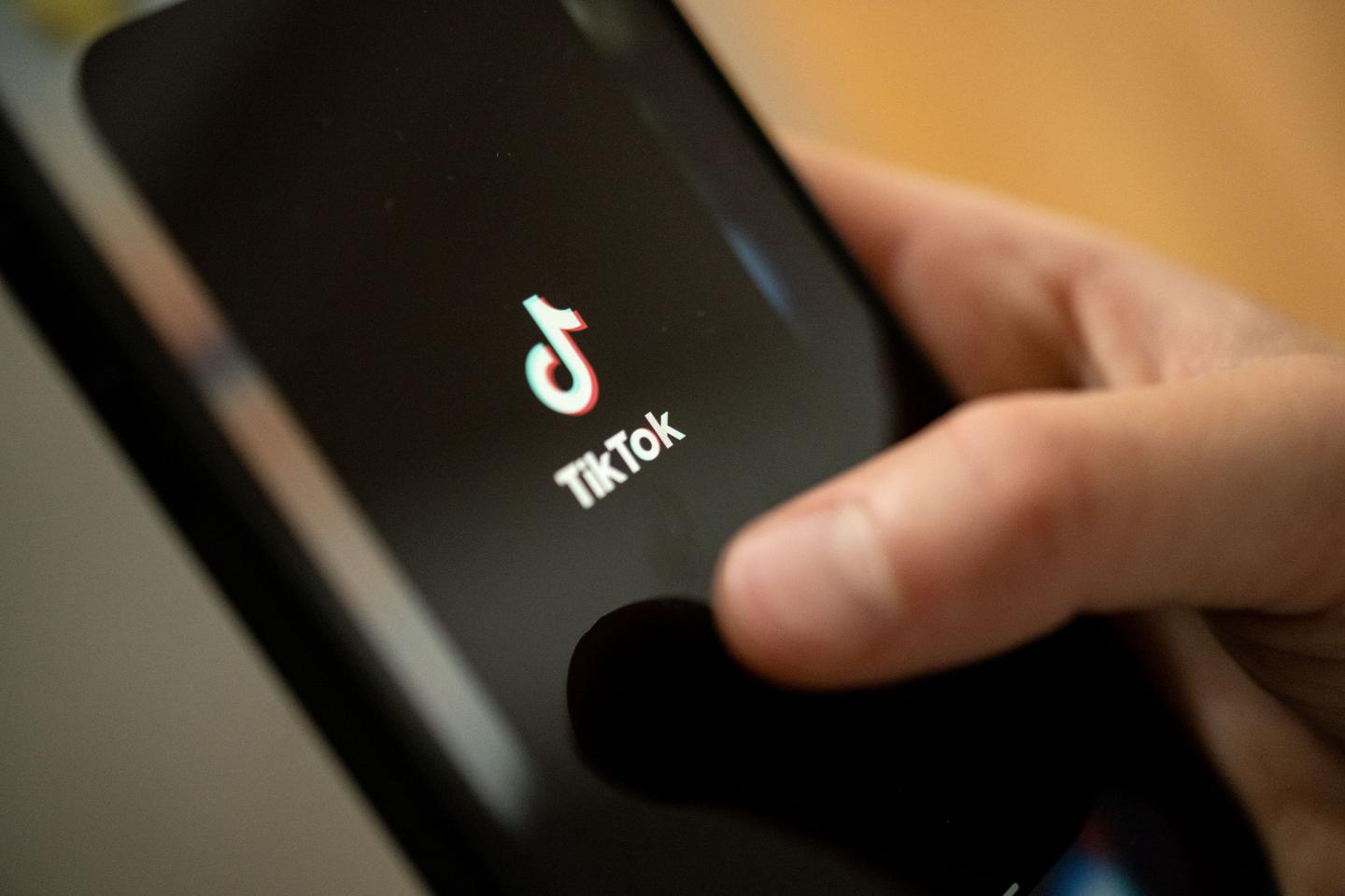 A person taps the TikTok logo on a smartphone.
