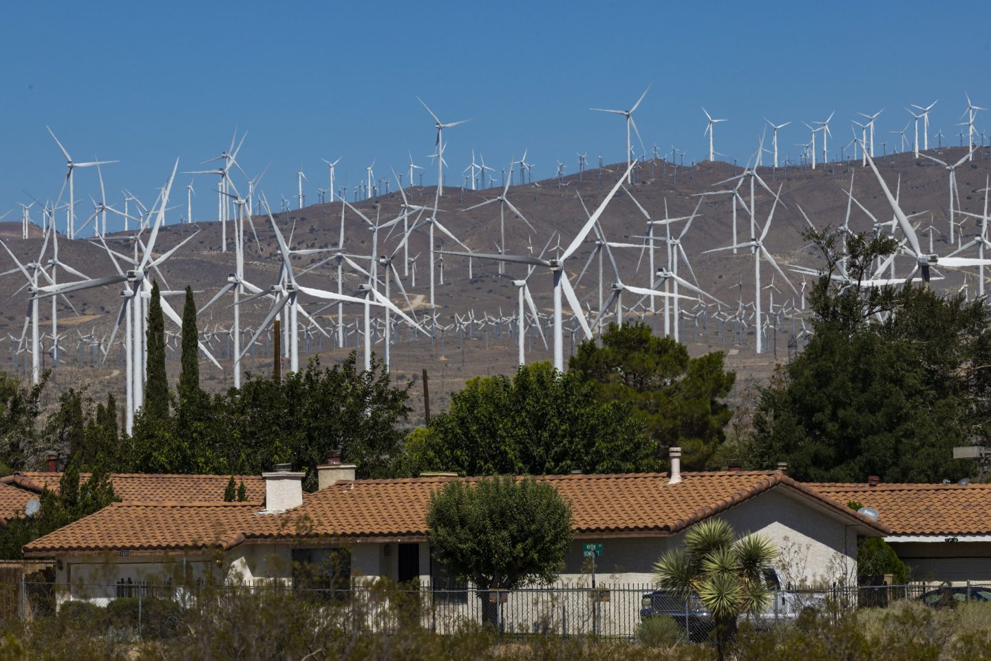 Wind turbines sprawl across the Mojave Desert next to a small community of homes in California.