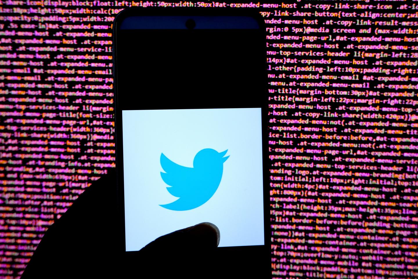 Twitter logo appearing on a phone screen in front of lines of code in the background