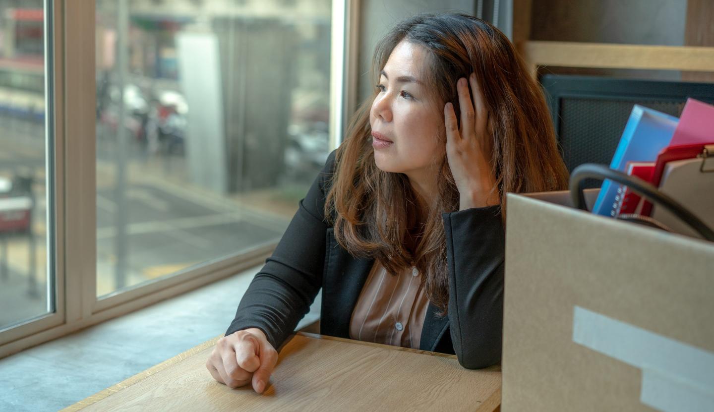 An Asian woman in the office thinking while looking out of the window daytime.