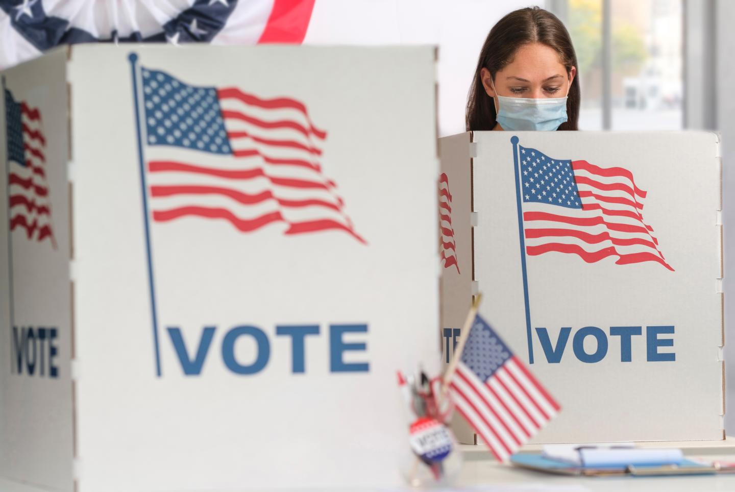 A white woman wearing a face mask voting behind a booth