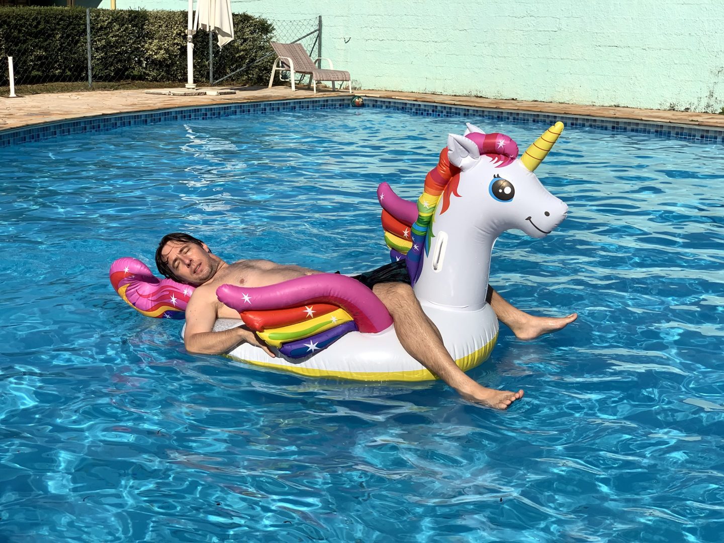 Man lying on a unicorn raft in a pool.