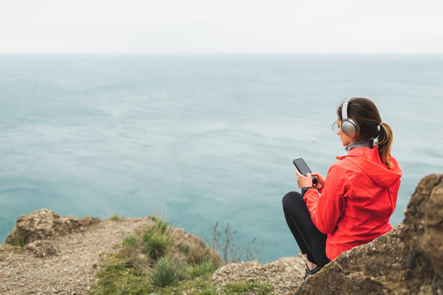 Woman in red jacket sitting on a trail looking at her phone