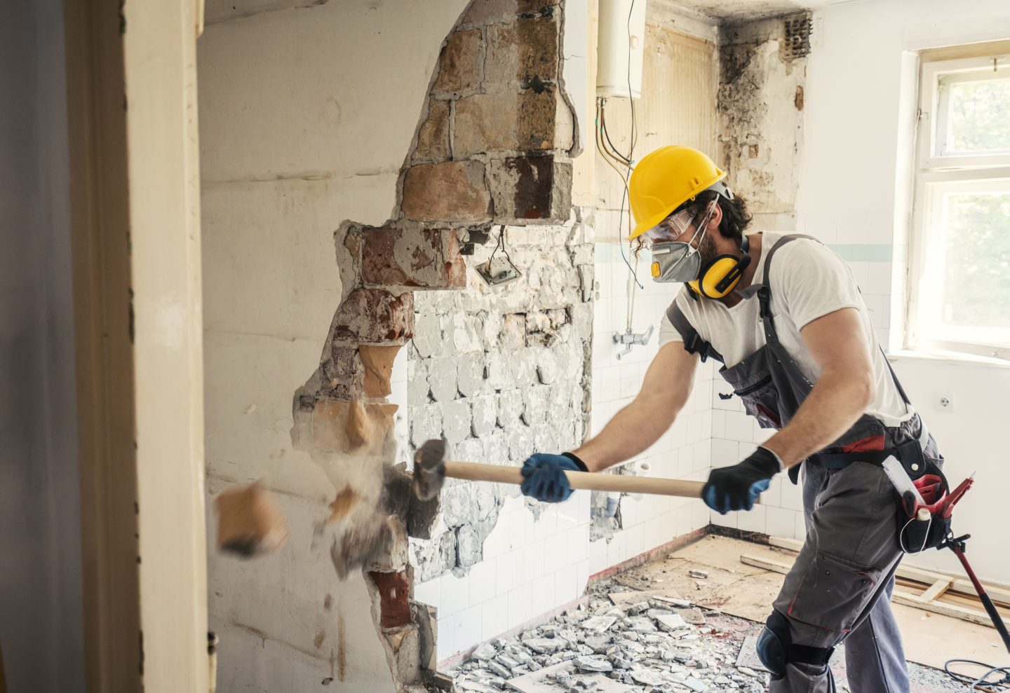 A worker demolishes an interior wall in a house.