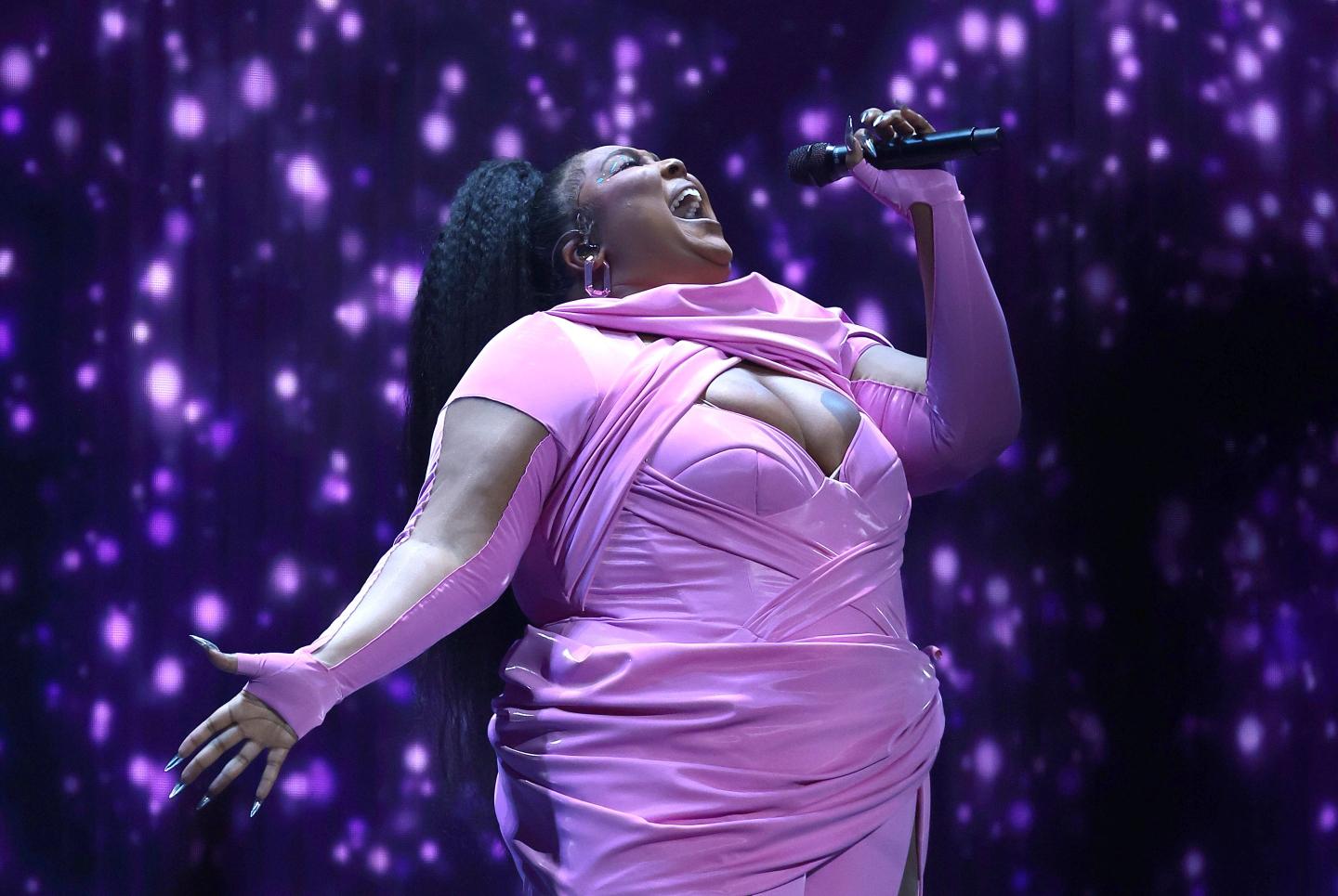 Lizzo holding a mic while singing on a stage.