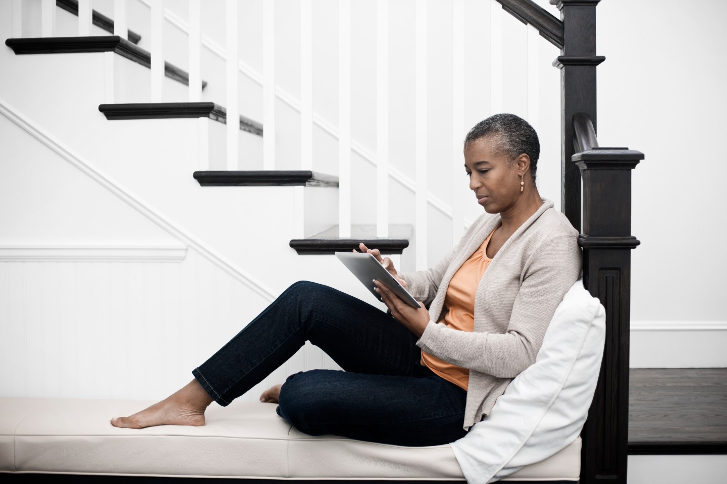 A mature woman seated in a hallway using a digital tablet.