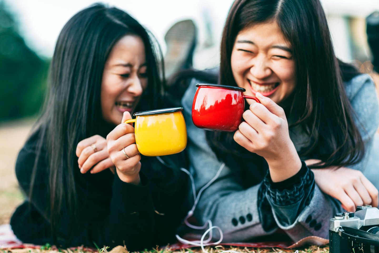 Two young Women Enjoying Hot Drink And Music In Park In Autumn