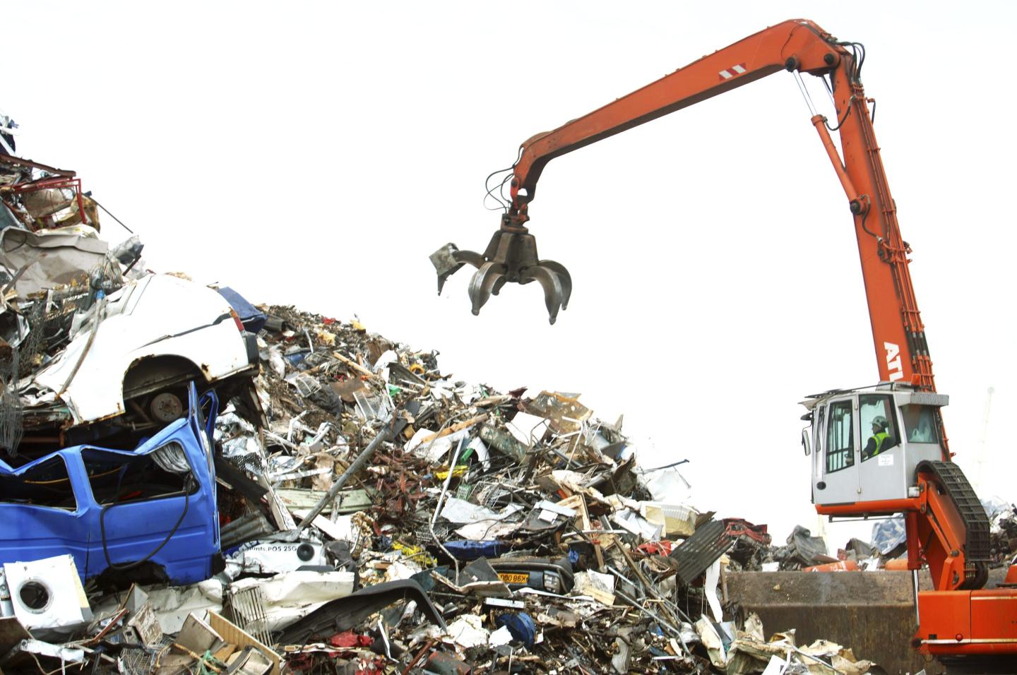 Mechanical loader with a grappling arm at a metal recycling facility on the dockside at a port in Newport, South Wales, UK